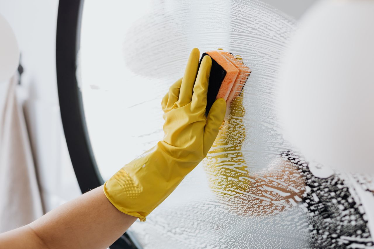 services-01 Anonymous person in yellow rubber gloves using simple sponge for cleaning mirror in bathroom